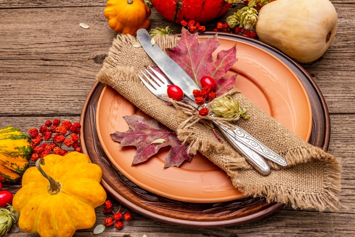 fall plate decorative dining set-up. On a dark brown wooden table, with berries and pumpkins surrounding it.